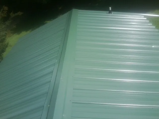 New green metal panels meeting at the ridge of a roof — Flat Roof Repair work by our crew in Marietta